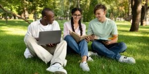 A number of students sitting outside, reviewing content on laptops and mobile devices